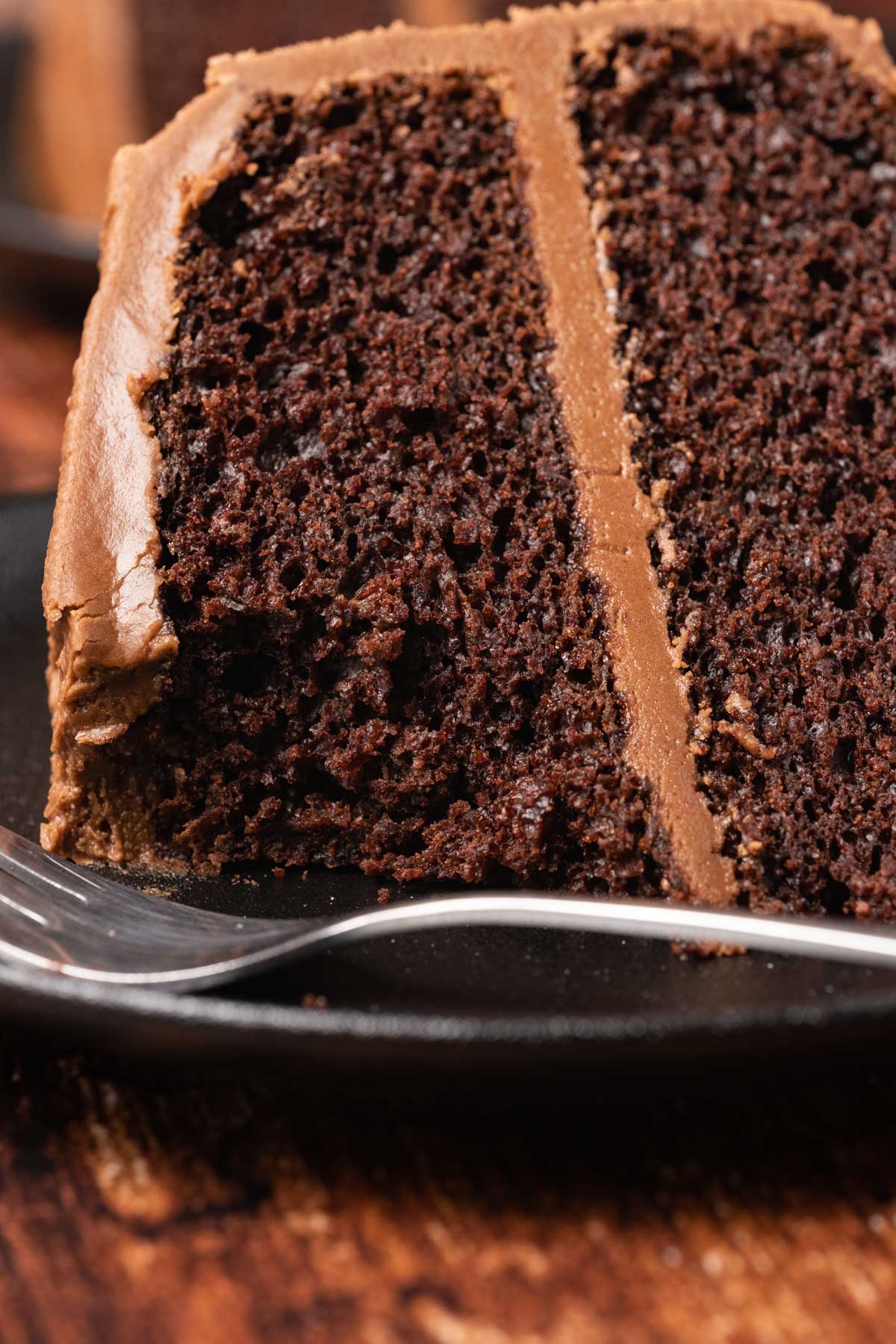 Slice of vegan chocolate cake on a plate with a cake fork. 