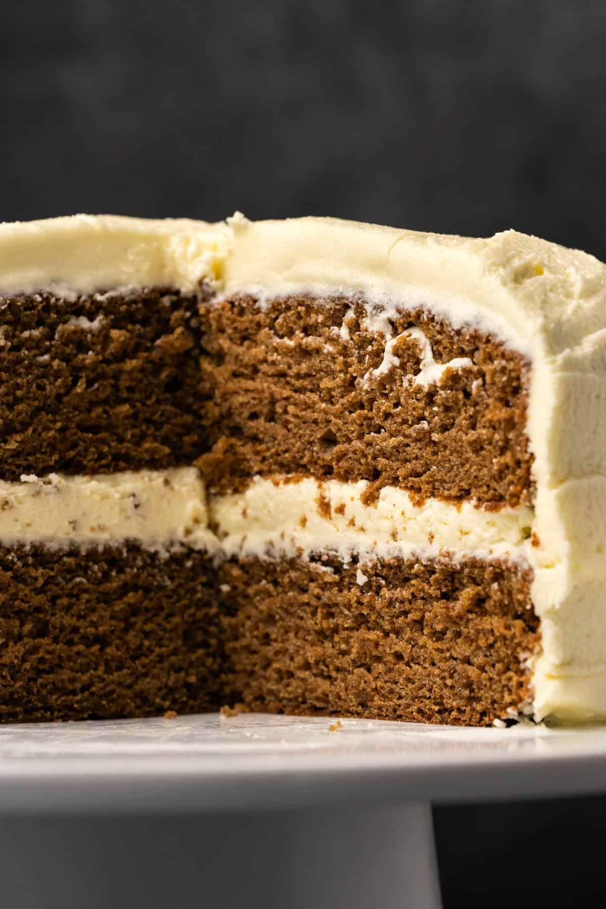 Vegan gingerbread cake with slices removed, on a white cake stand. 