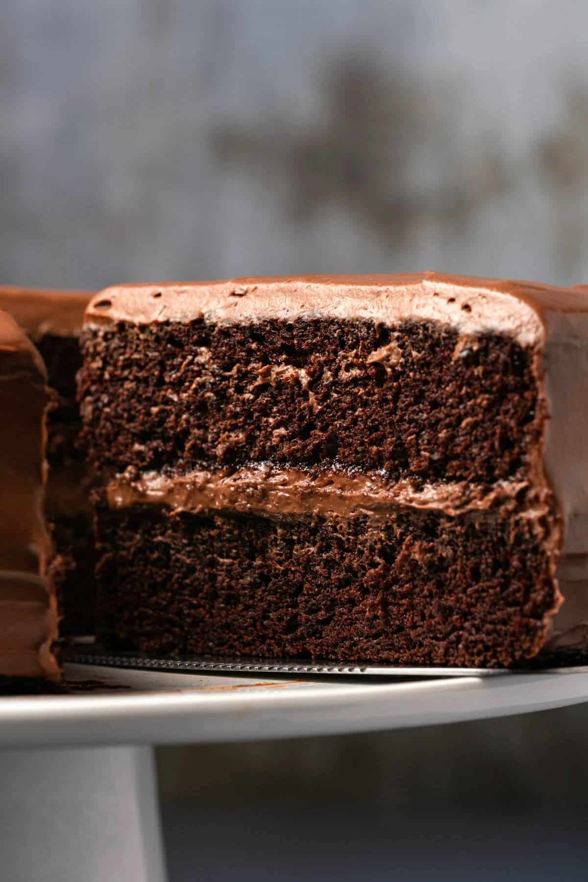 Vegan gluten free chocolate cake on a white cake stand with one slice cut and ready to serve. 