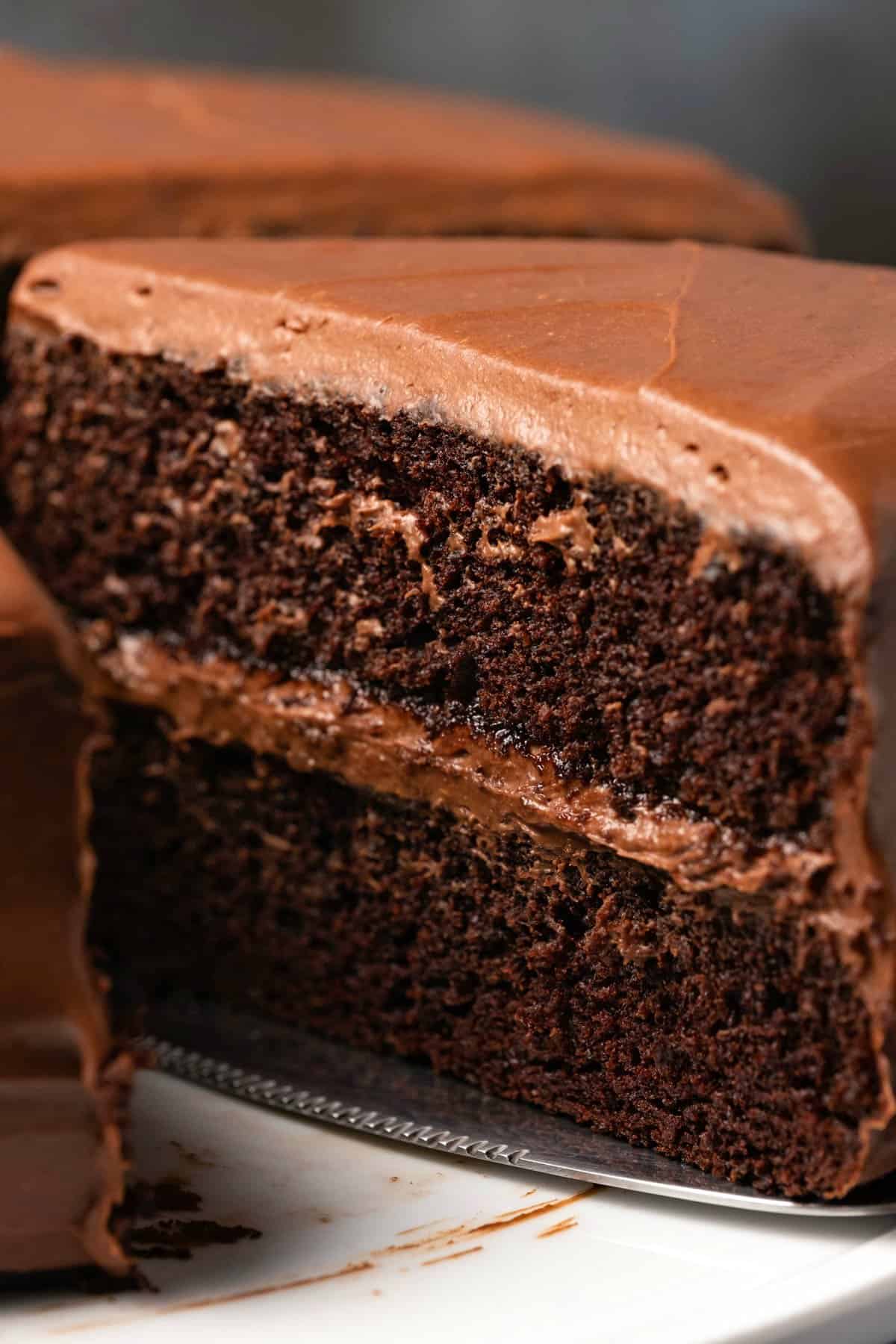 Vegan chocolate cake on a white cake stand with one slice cut and ready to serve. 