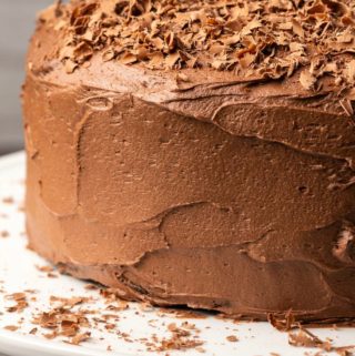 Cake frosted with vegan chocolate buttercream frosting on a white cake stand.