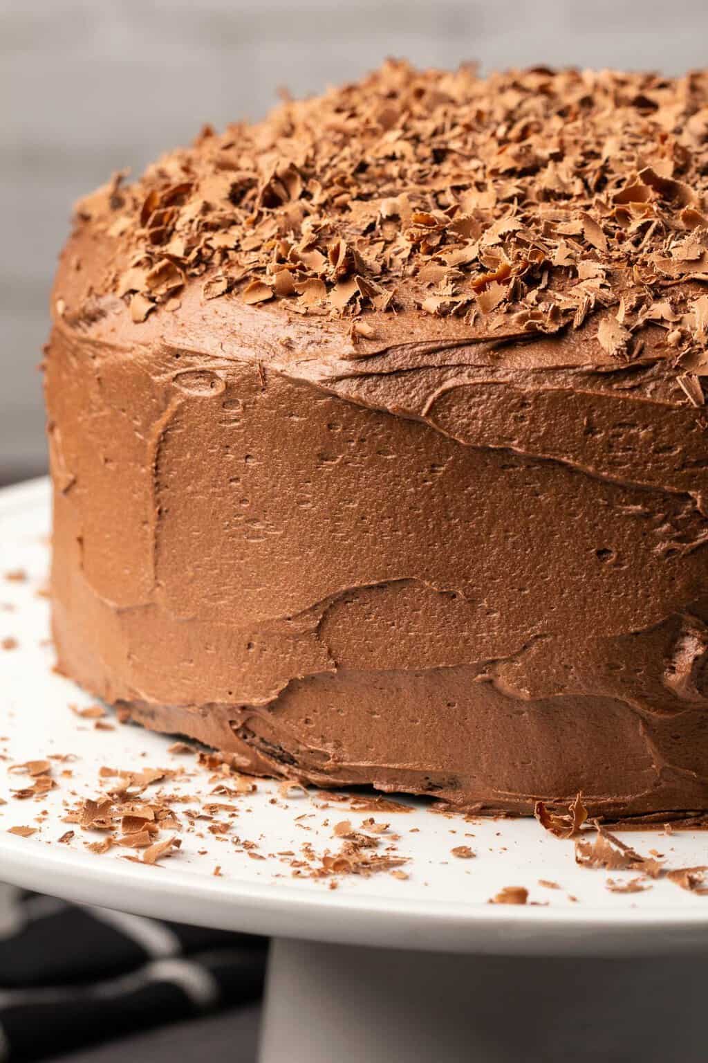 Frosted chocolate cake on a white cake stand. 