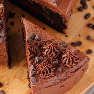 Vegan chocolate zucchini cake with a slice cut on a round wooden board.