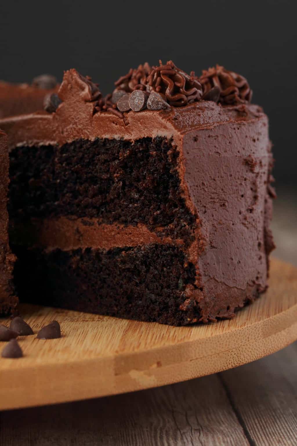 Vegan chocolate zucchini cake on a wooden board with one slice cut and ready to be served. 