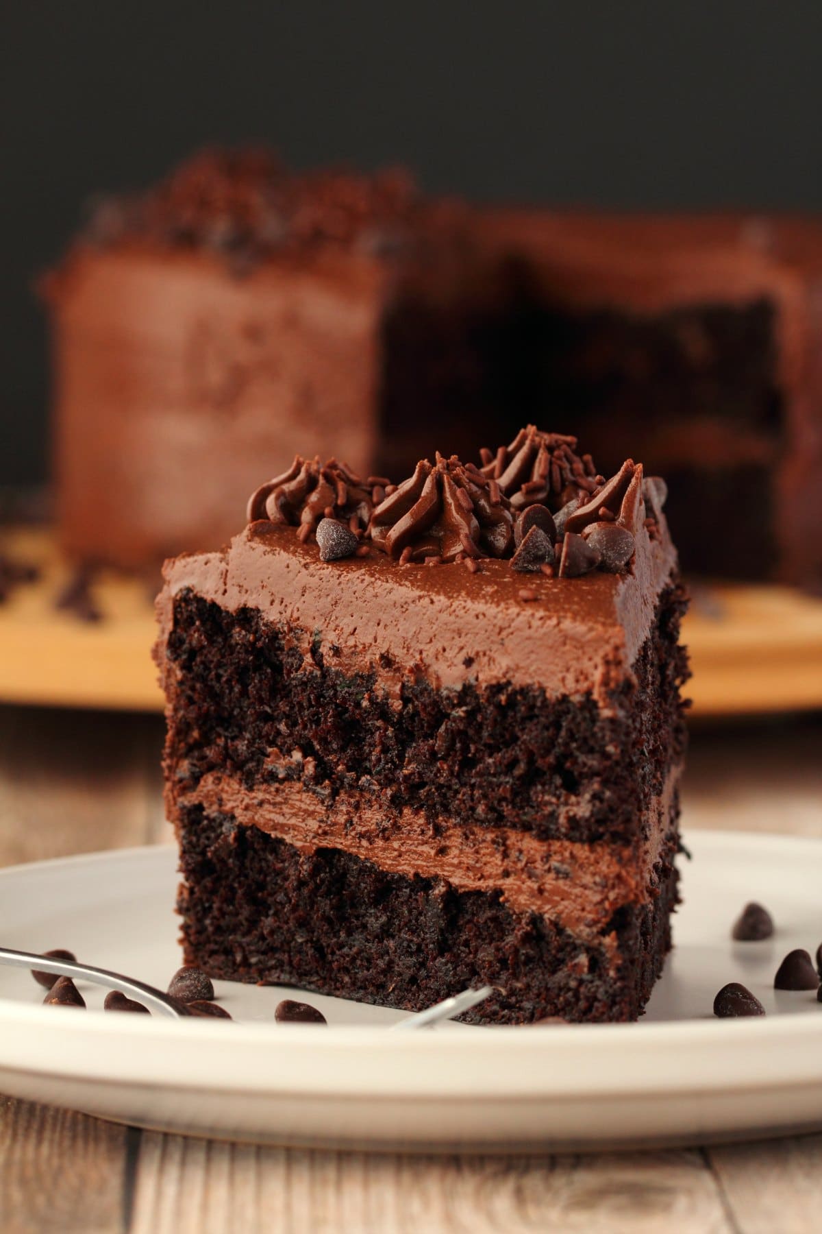 A slice of vegan chocolate zucchini cake on a white plate with chocolate chips and a cake fork. 