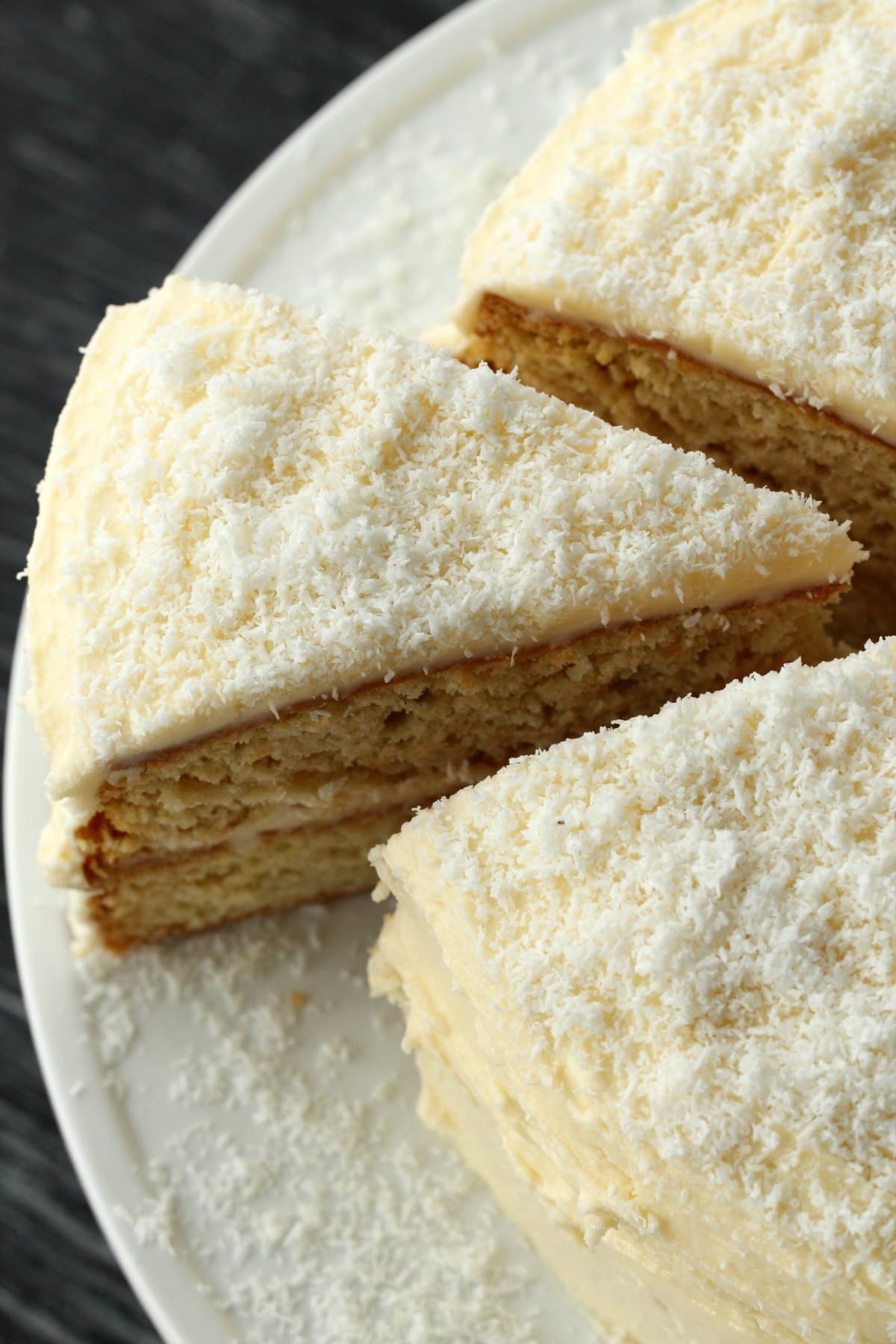 Frosted cake on a white cake stand with one slice cut and ready to be served. 