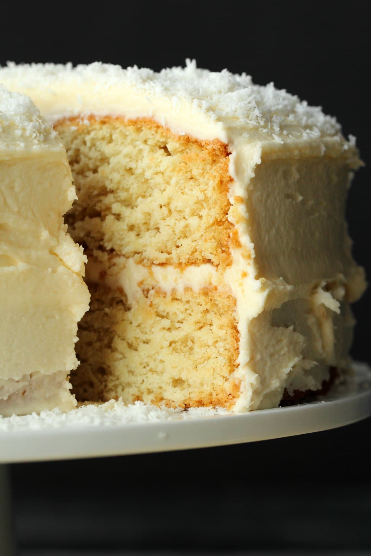 Vegan coconut cake on a white cake stand with one slice cut and ready to be served. 