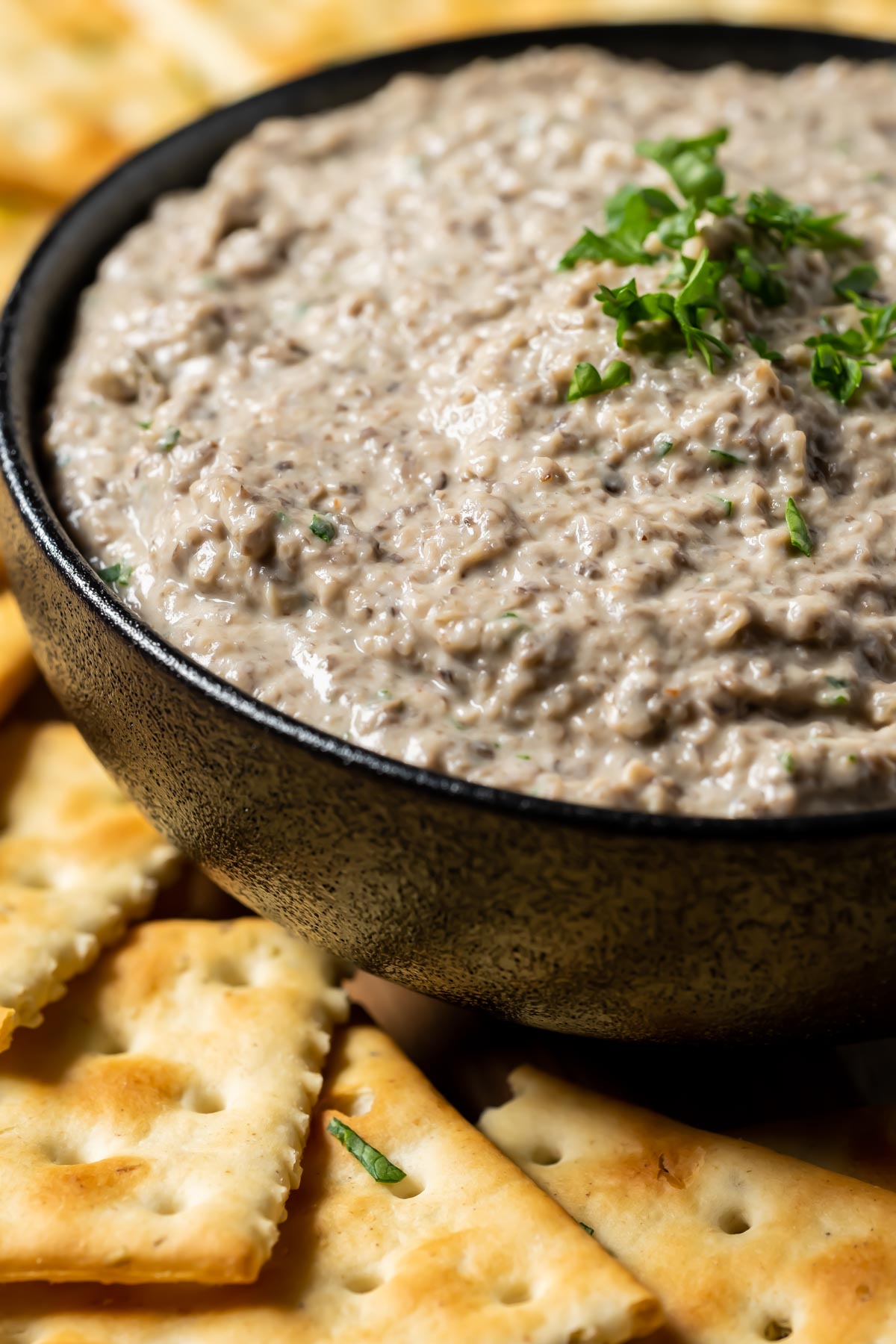 Vegan mushroom pâté in a black bowl with crackers.