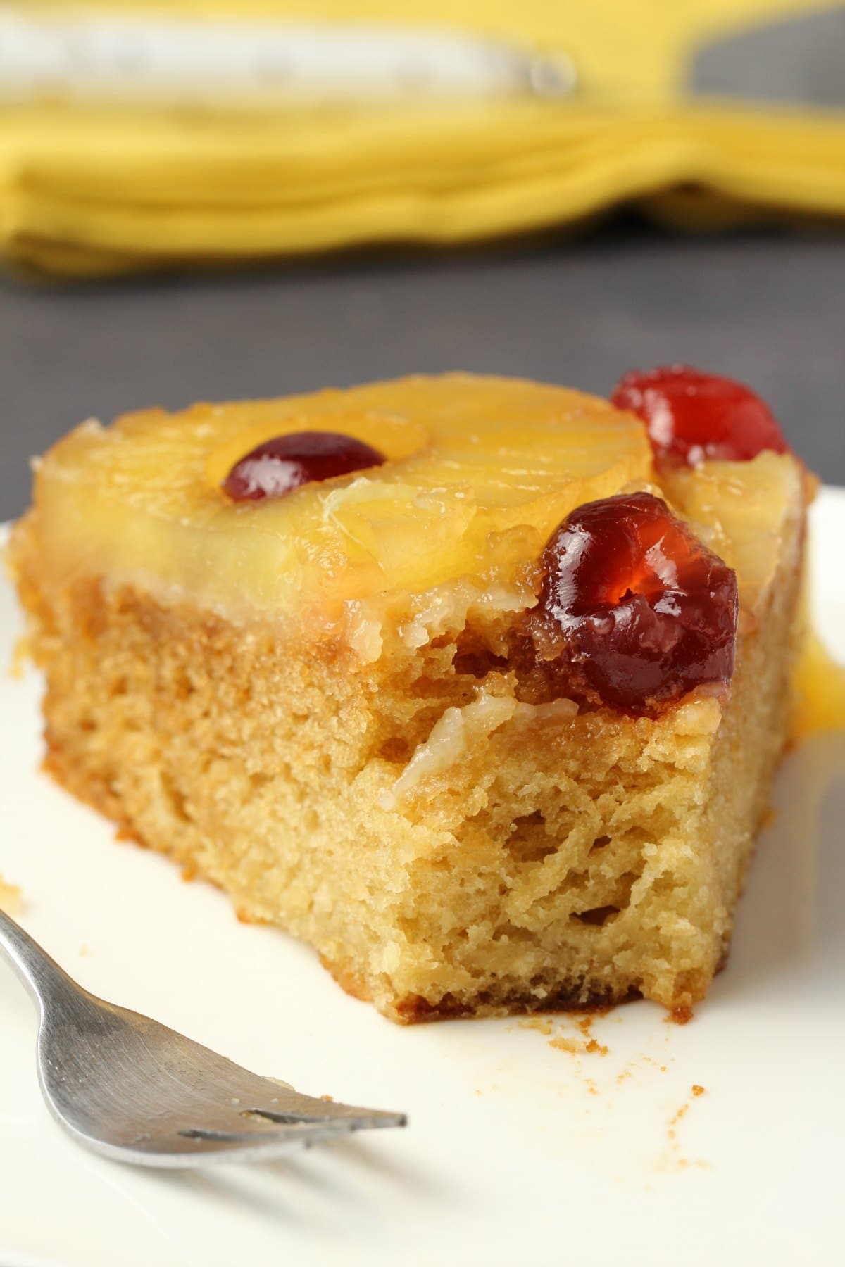 A slice of vegan pineapple upside down cake on a white plate with a cake fork. 