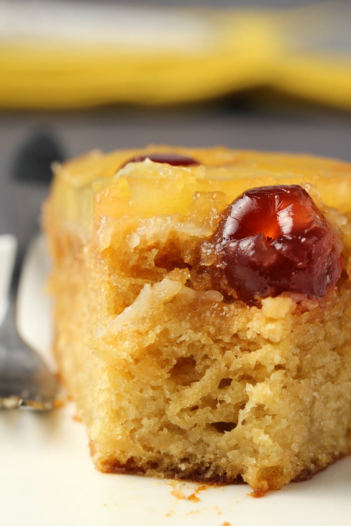 A slice of vegan pineapple upside down cake on a white plate with a cake fork. 