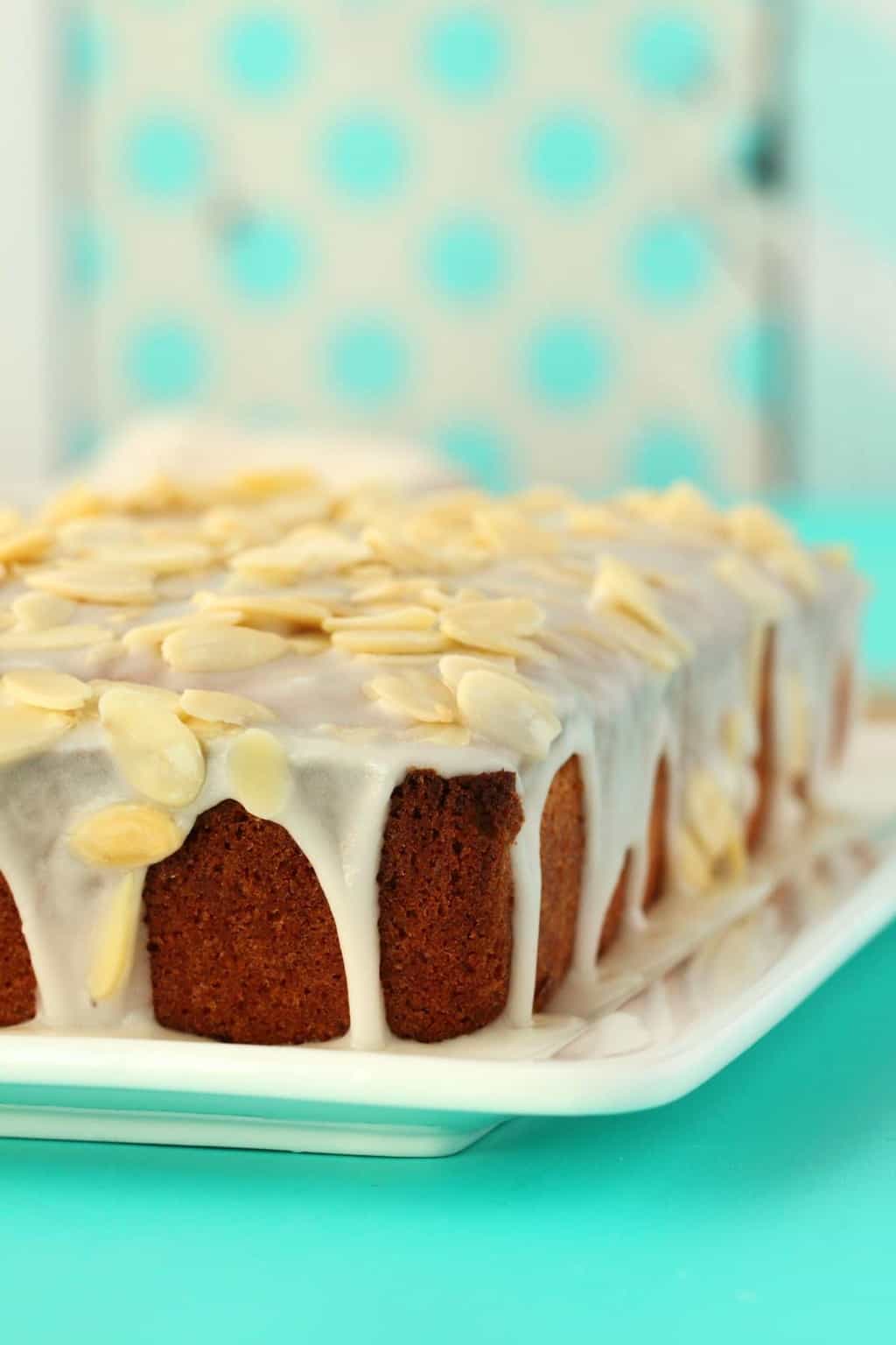 Vegan Pound Cake topped with an almond glaze and almond flakes on a white plate. 