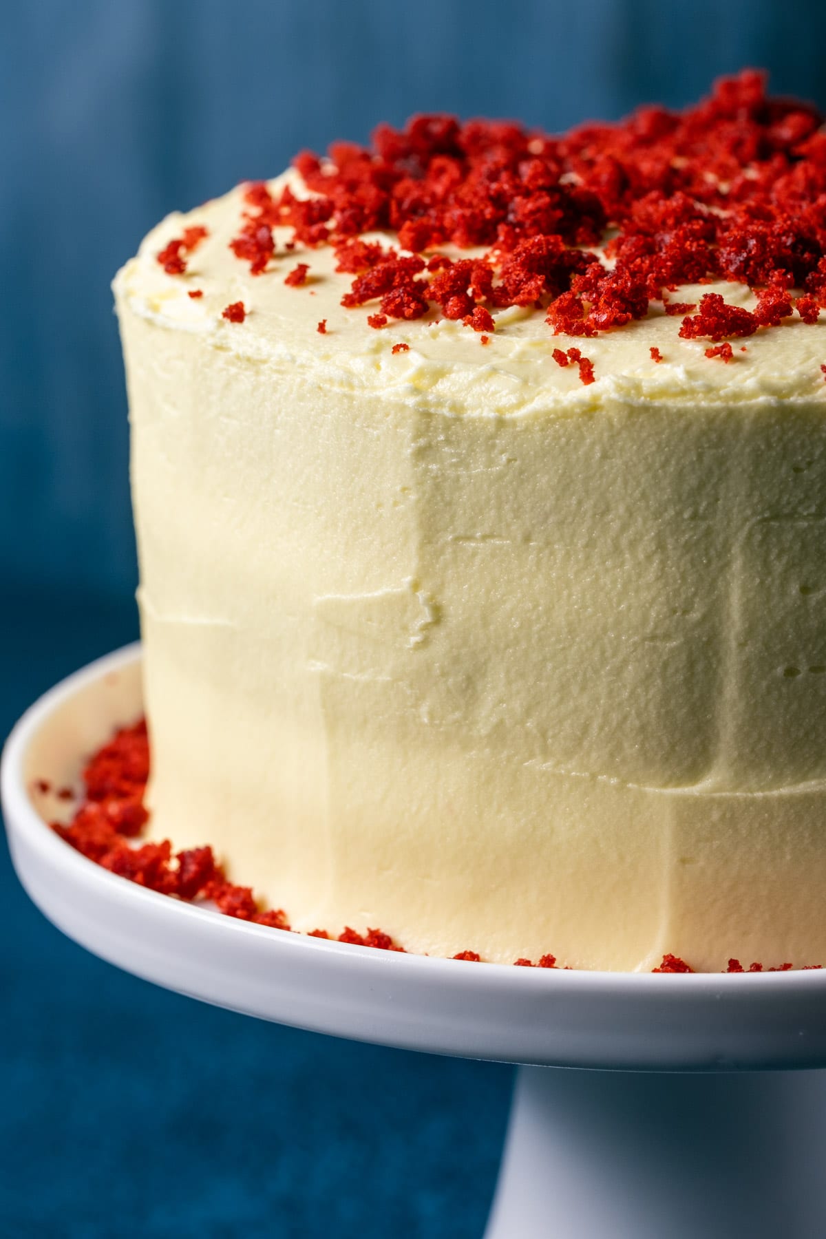 Frosted and decorated vegan red velvet cake on a white cake stand.